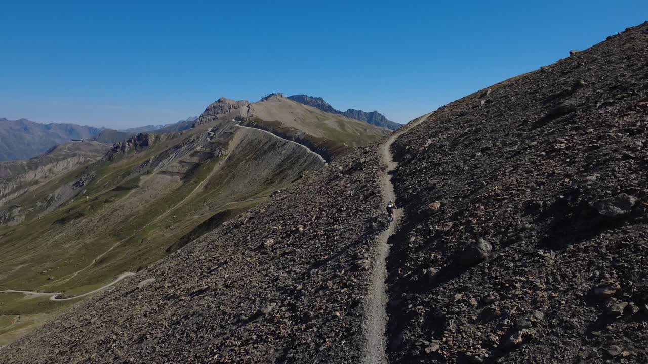 Energetic drone shot of cyclists powering uphill on a winding gravel trail in the Austrian Alps. Perfect for sports, endurance, and adventure content