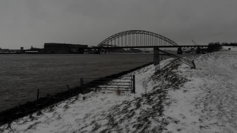 snowy riverside of noord with a bridge on the background in netherlands. - aerial, black and white