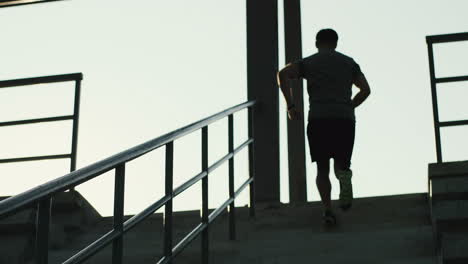 rear view of young jogger man running up the stairs in the stadium on a summer day