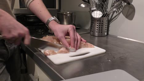 persona caucásica cortando pechuga de pollo para la cena