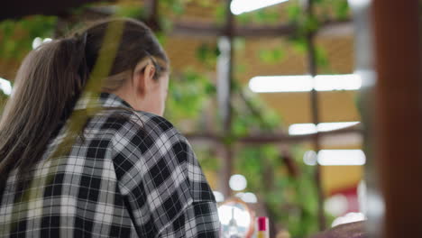 vista aérea de una mujer aplicando maquillaje usando esponja de belleza en un espacio suavemente iluminado, espejo y productos cosméticos dispuestos en la mesa, rodeados de vegetación, momento de relajación y cuidado personal capturado desde arriba