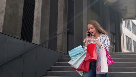 girl walking from shopping mall with shopping bags and talking on mobile phone about purchases