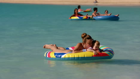 a mother and baby floating in clear blue water at a beach