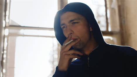 A-Young-Man-In-A-Hood-Smoking-A-Cigarette-In-An-Abandoned-House-Near-The-Window