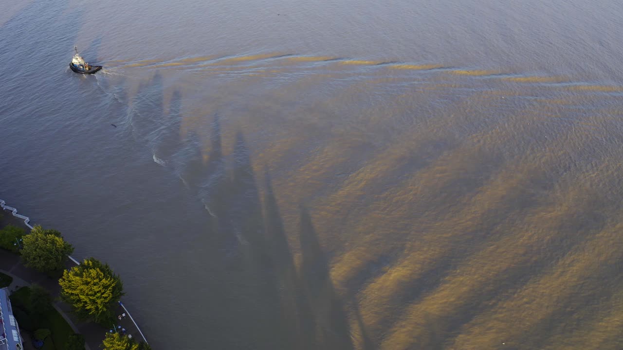 상업 강을 지나가는 공중 조감도 예인선은 황혼의 일몰 진흙 투성이의 물에 파도를 일으키고 항구 부두로 돌아가 고급스러운 주거용 보드워크 커뮤니티를 통과합니다.