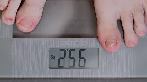 close up shot of man stepping on a home scale, checking his weight, and stepping back off