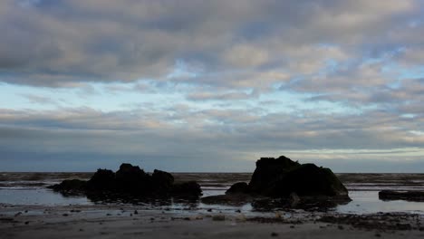 Low-angle-view-from-the-sandy-beach-on-the-rock-and-waves,-cloudy-sky-in-Dundalk,-Ireland