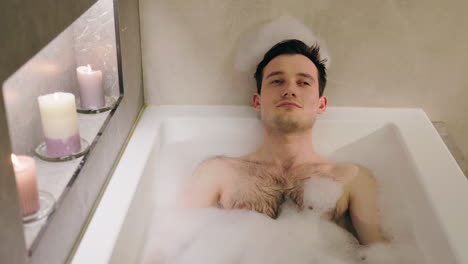 man relaxing in a warm bath with candles