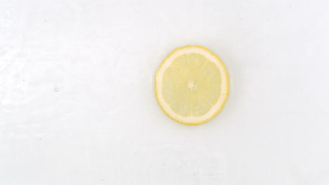 On-a-white-background-a-splash-of-water-falls-on-a-slice-of-lemon-in-slow-motion.