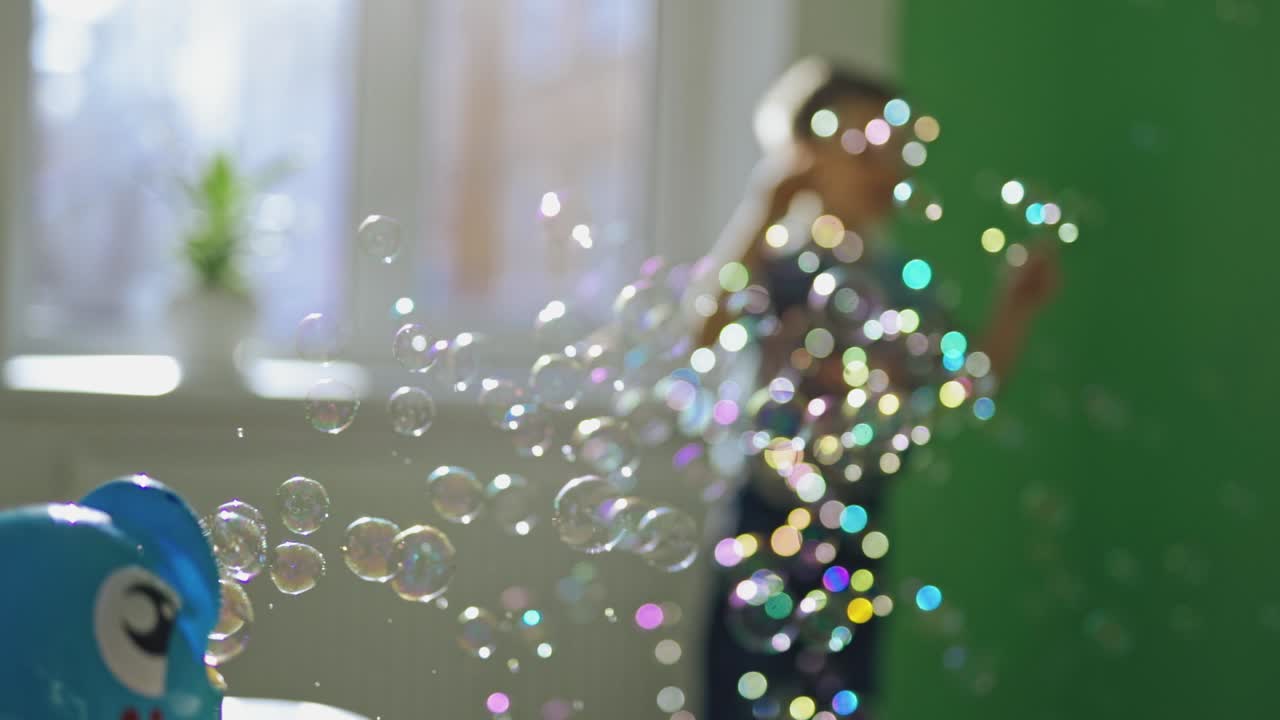 Many colorful bubbles flying in the room and a little boy playing with them. Joyful boy jumping happily and playing with soapy bubbles indoors. Soap bubbles show and a happy boy.