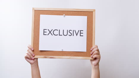 Woman's-hand-shows-the-paper-on-board-with-the-word-EXCLUSIVE-in-white-studio-background-with-copy-space