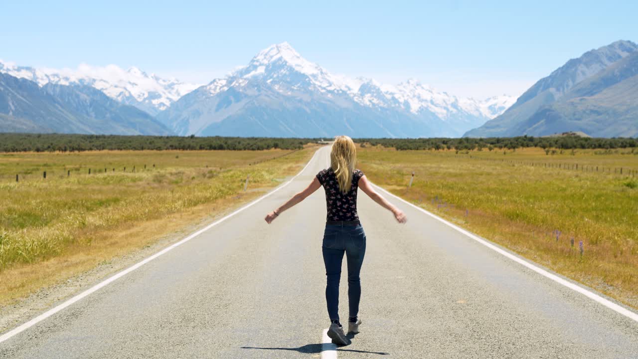 Rear view of a tourist girl enjoying famous State Highway 80 next to lake Pukaki overlooking Mt