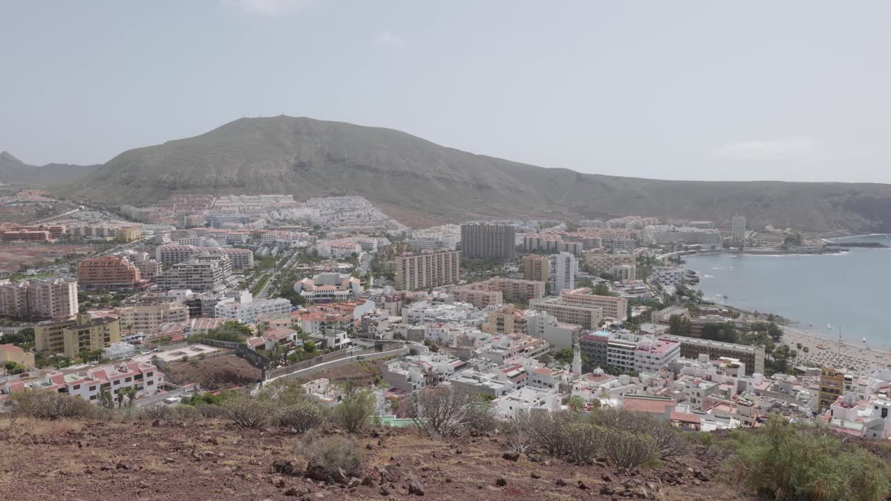 View of a town and hotels by the ocean and mountains in Los Cristianos, Tenerife, Canary Islands, Spain.