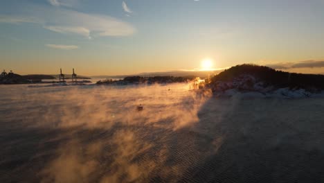 Puesta-De-Sol-De-Hora-Dorada-En-El-Horizonte-Cerca-De-Bjorvika,-Oslo-Durante-El-Invierno-Con-Niebla-Flotando-Sobre-El-Agua