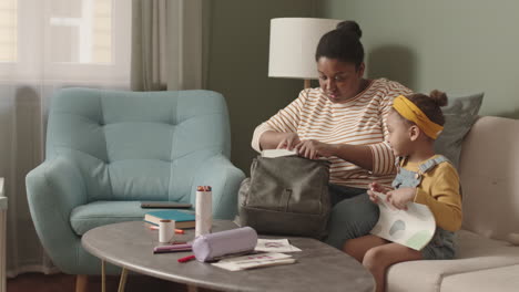 mother helping schoolchild packing school bag
