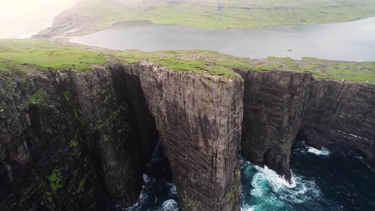 Drone pull out view of towering sea cliffs along the Algarve coast near Sagres, Portugal, showing rugged rock formations, crashing waves below, and expansive coastal landscape