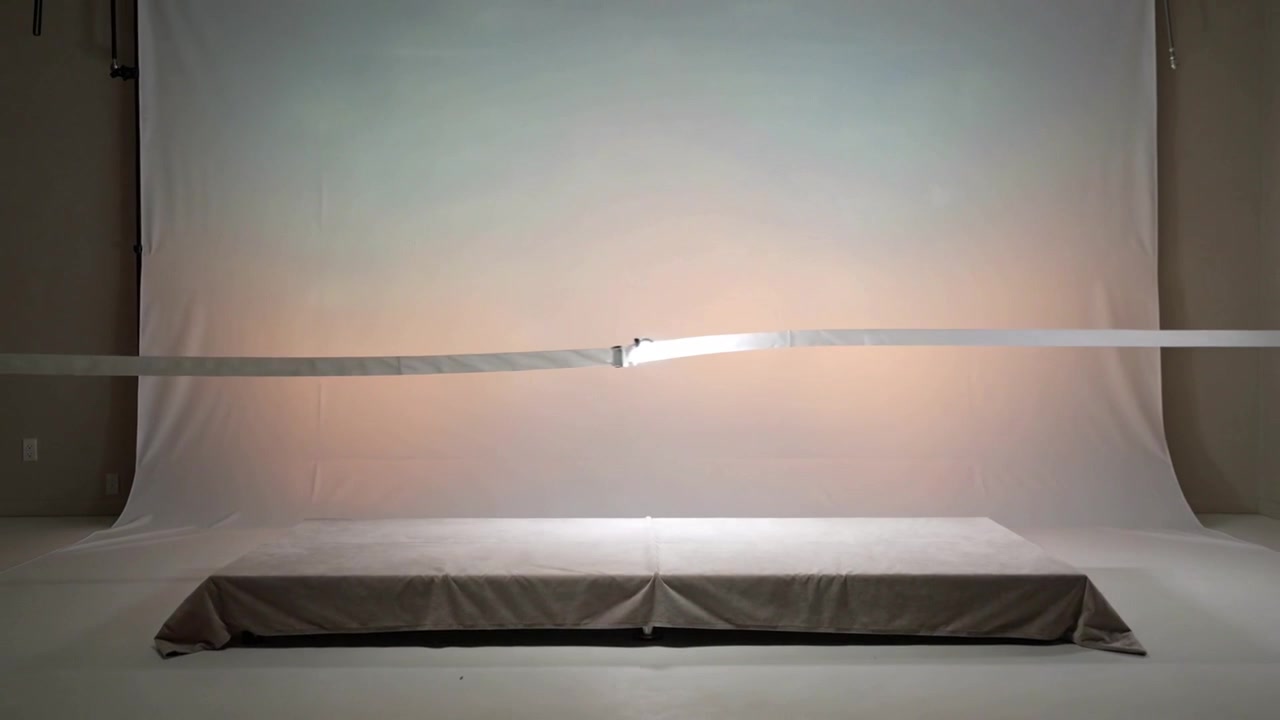 Sliding reflective strip with clasp shifting right across studio backdrop by off-frame rig to level