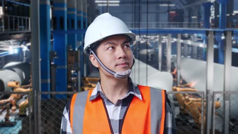 primer plano de un ingeniero asiático con casco de seguridad de pie en una fábrica de fabricación de turbinas eólicas. mirando a su alrededor, comprobando