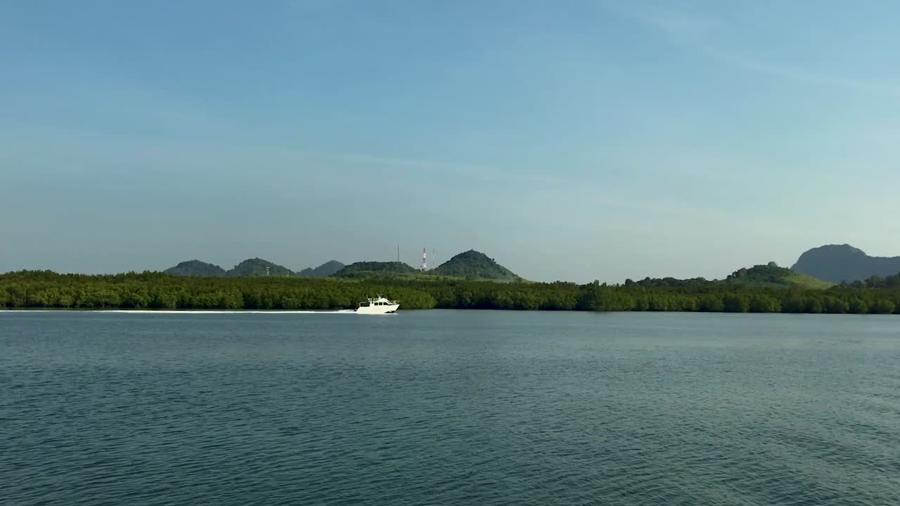 Panning shot of bright white boat speeding next to an island in Thailand