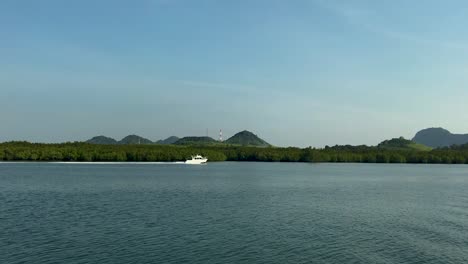panning shot of bright white boat speeding next to an island in thailand