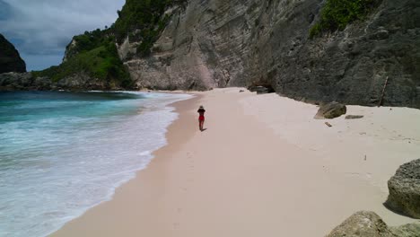 young asian female model walking gracefully on a white sand beach with the waves crashing at nusa penida diamond beach in bali indonesia on a sunny tropical day