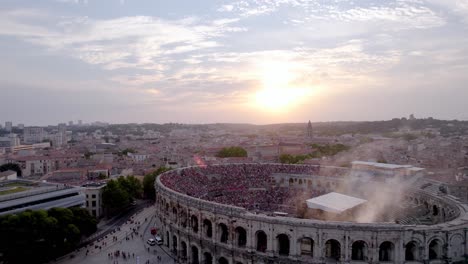 Drone-over-the-Arena-of-Nîmes-at-sunset-with-smoke,-people-are-waiting-for-the-stromae-concert