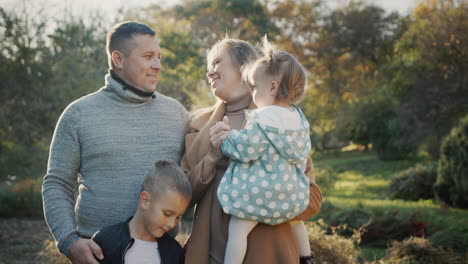 portrait of a young healthy family - a couple with two children. smiling, looking at the camera. standing in the autumn park