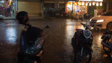 busy street in thailand with rain pouring down as traffic passes by an open restaurant at night