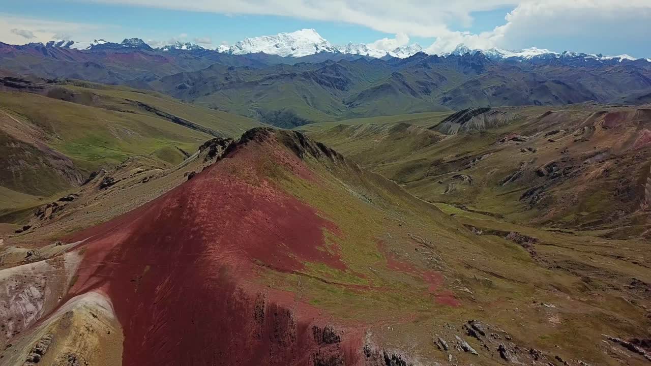 Aerial, tilt up, drone shot revealing a red peak and geological formations, snowy mountains in the background, in Valle Rojo Valley, Andes, Peru, South America