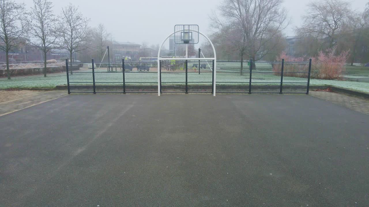 霧に覆われた公園にある都市のバスケットボールコートへ向かって飛ぶドローン