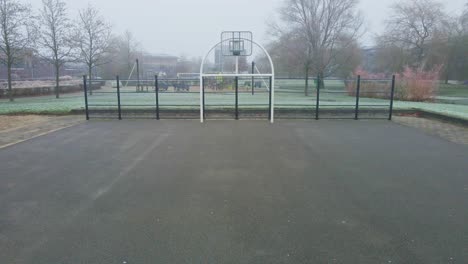 Drone-flying-towards-urban-basket-ball-court-in-a-mist-covered-park