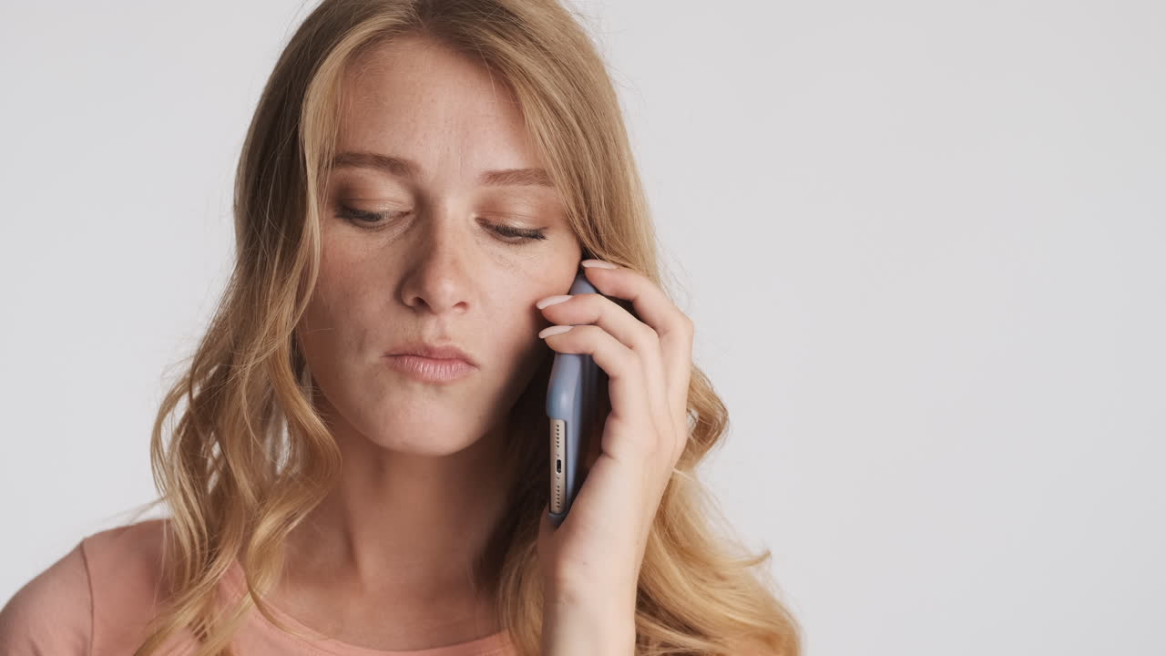 Caucasian woman chewing a gum while talking on the phone on camera.