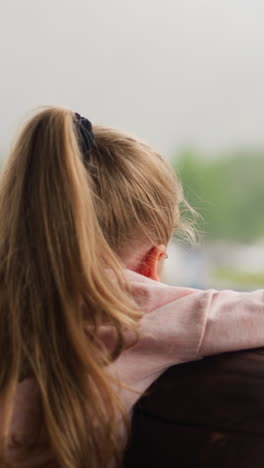 adorable little girl leans on log handrail and watches helicopter starting engine from terrace of resort cafe on rainy day slow motion