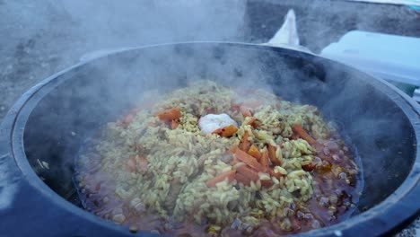 A-large-pot-of-pilaf-simmers-over-an-open-fire-in-Crimea,-Russia,-with-steam-rising-from-the-dish