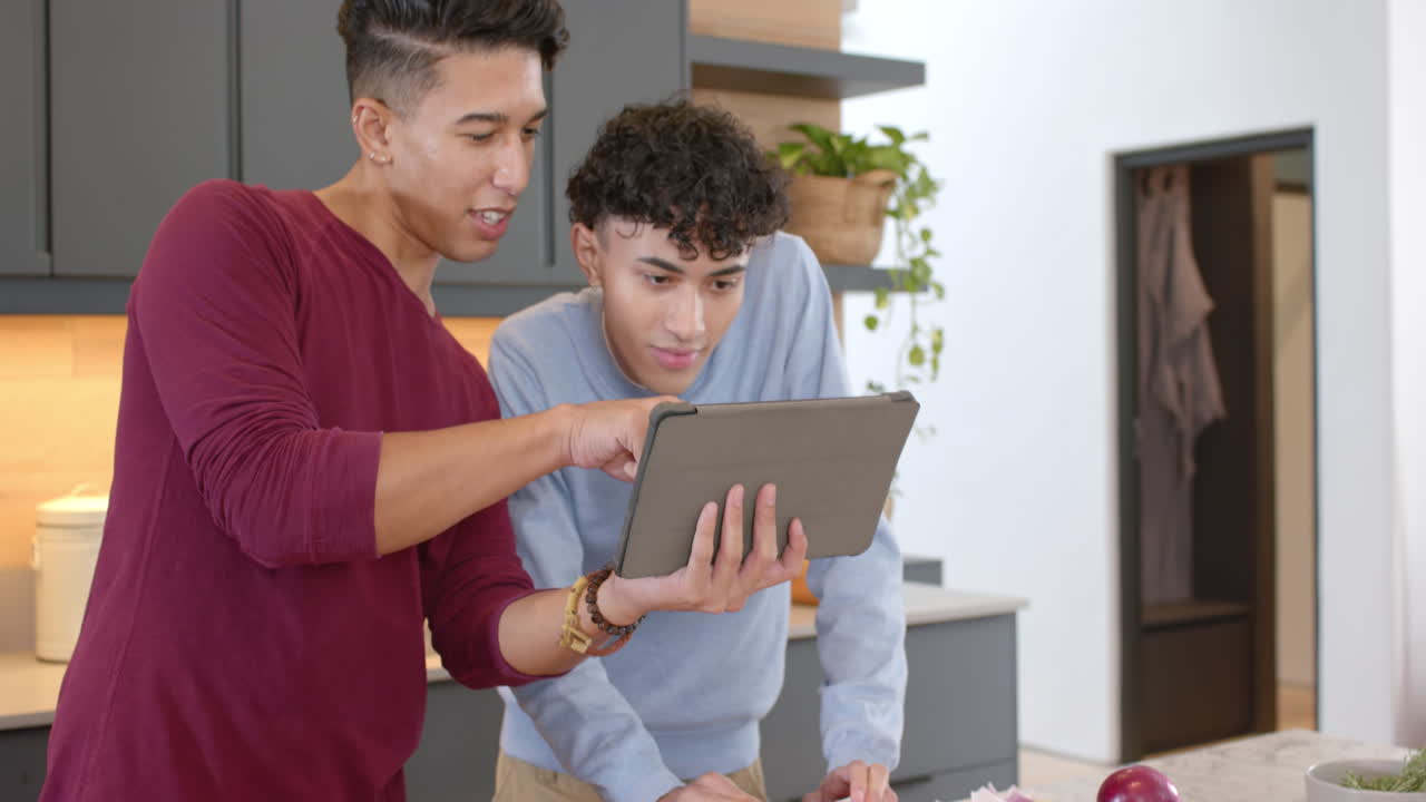 Cooking together in modern kitchen, multiracial gay couple using tablet, at home