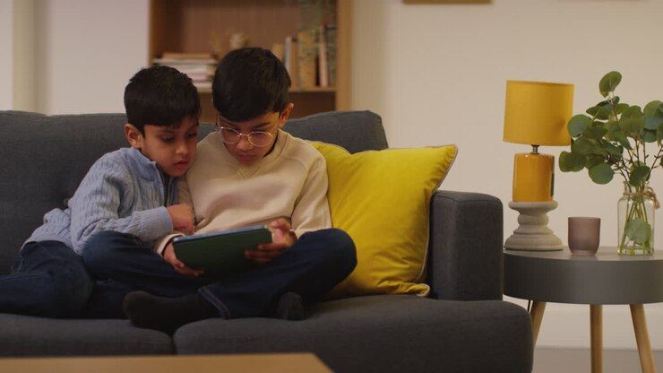 Due ragazzi giovani seduti sul divano a casa che giocano o guardano contenuti in streaming su un tablet digitale 9