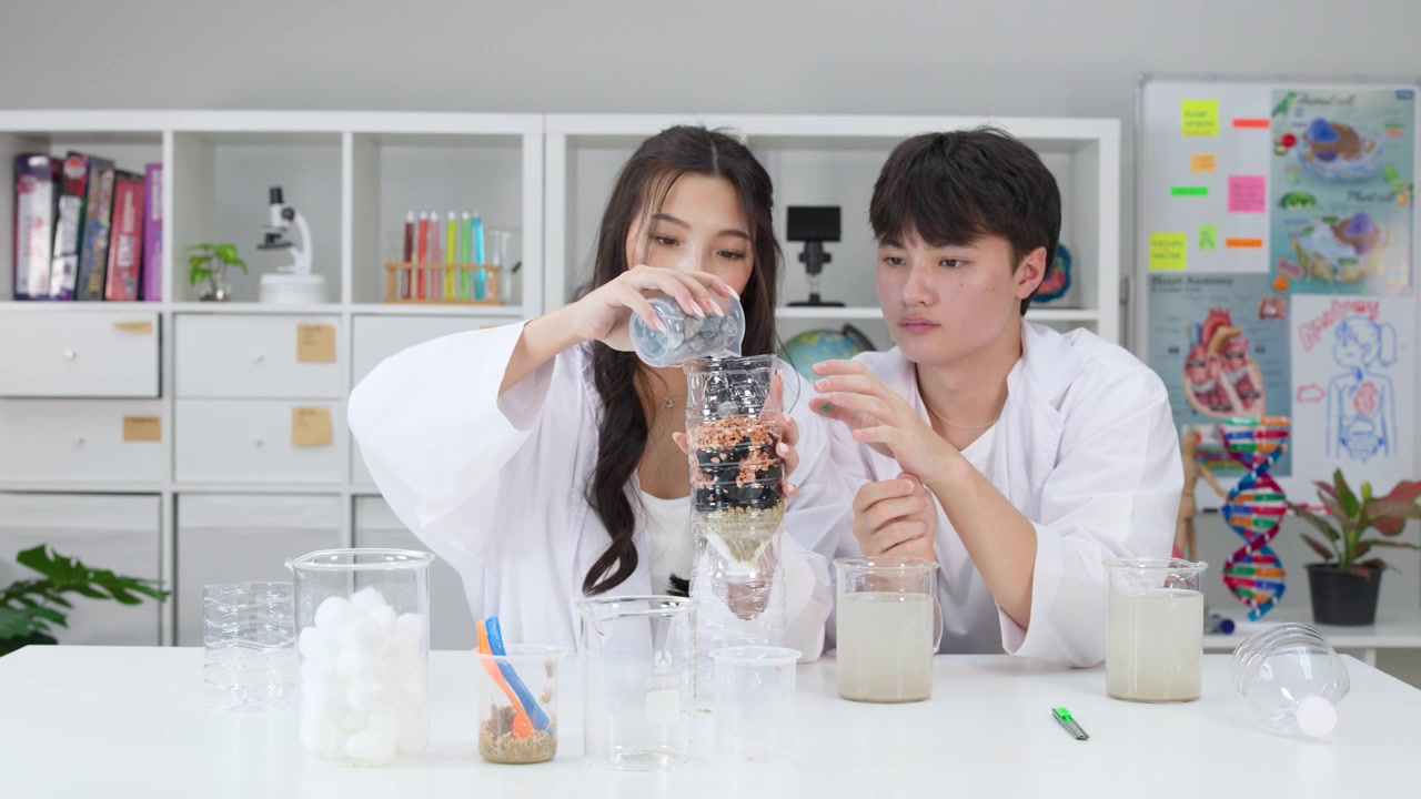 理科の授業中、白衣を着た2人の生徒がDIYフィルターを通して汚れた水を注ぐ。
