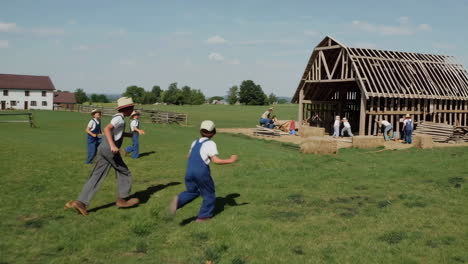 children working and playing around a wooden barn structure in a rural setting