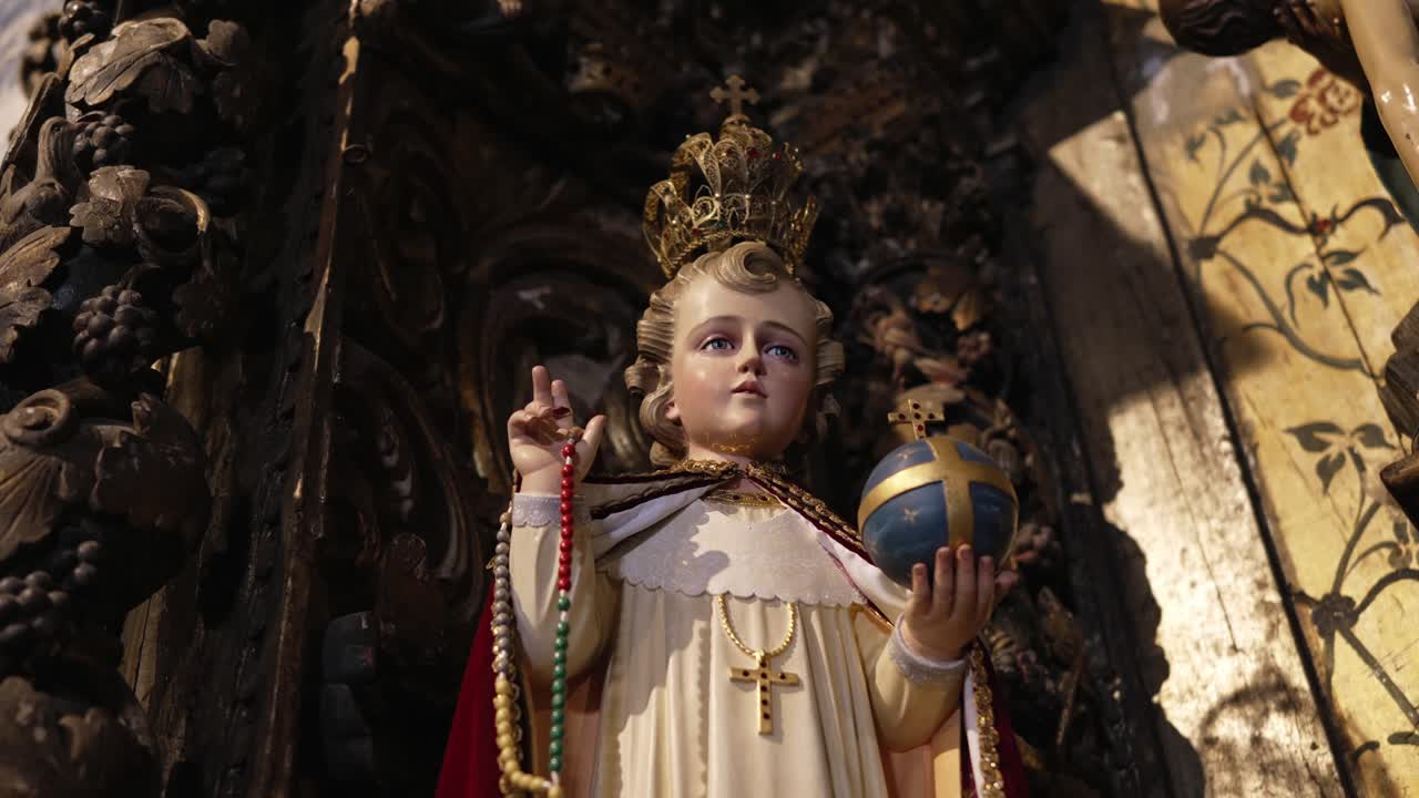 Sculpture of Child Jesus crowned, holding a globe and rosary, surrounded by intricate carvings