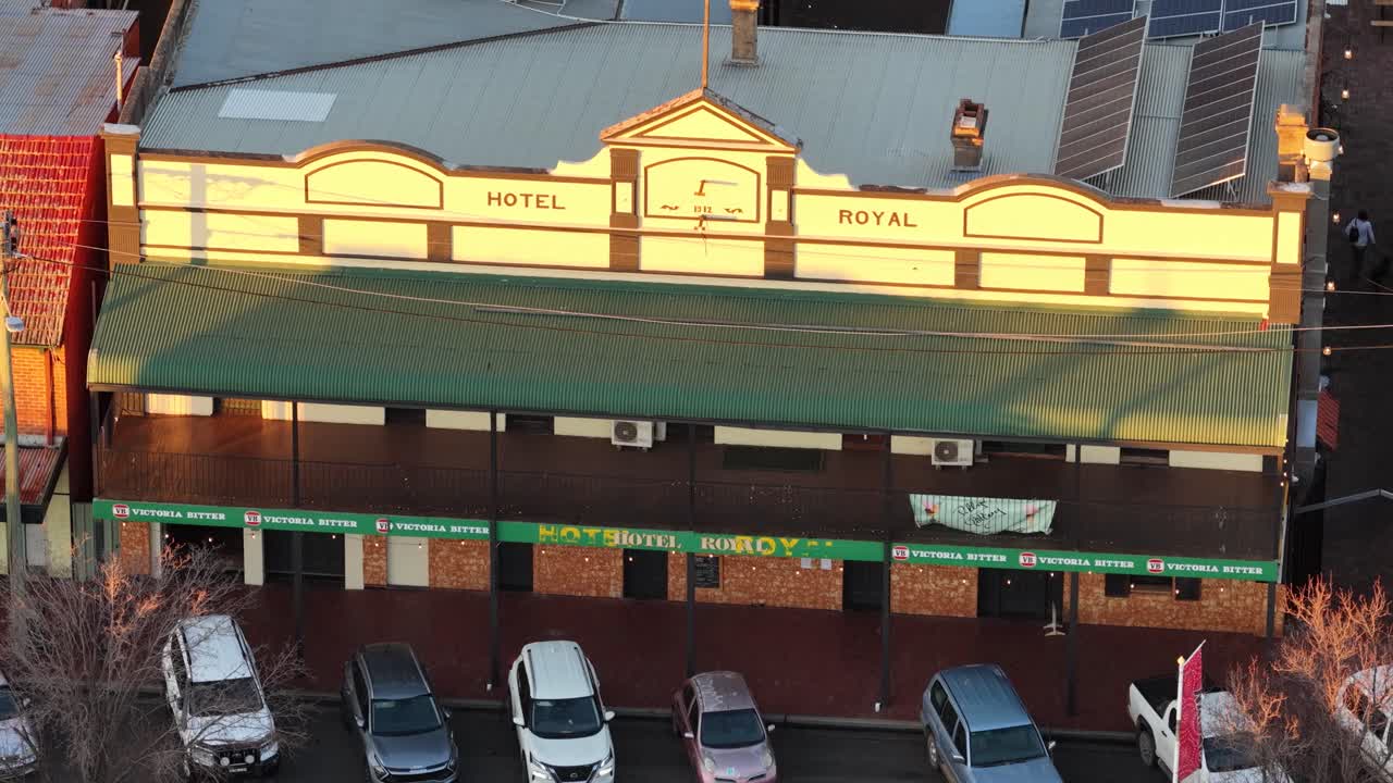 Aerial camera slowly pans across the Royal Hotel facade in Coonabarabran, New South Wales, with warm sunset lighting and parked cars below