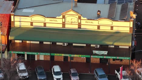 aerial camera slowly pans across the royal hotel facade in coonabarabran, new south wales, with warm sunset lighting and parked cars below