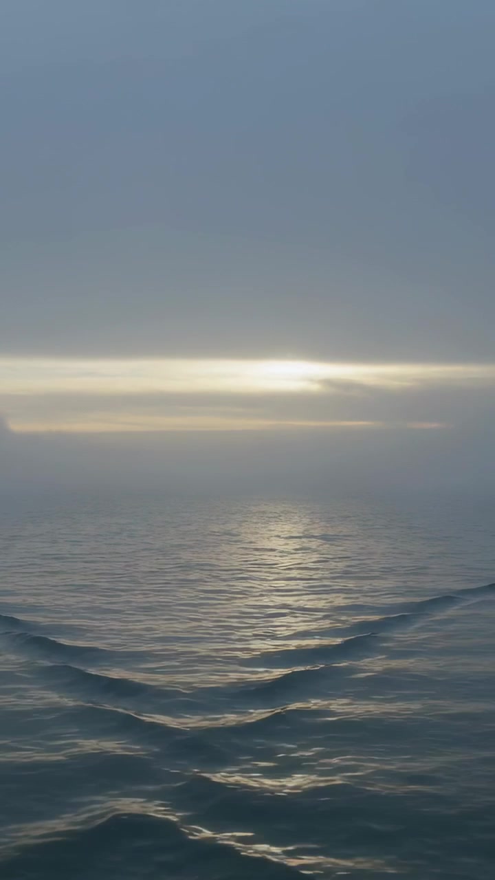 Vertical video: Rolling sea surface crests responding to low horizon light and breeze at sea
