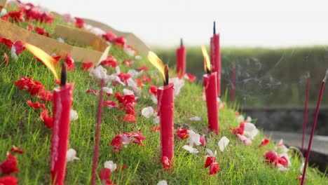 red candles burning on grassy grave with ornamental colorful flowers, chinese qingming tomb-sweeping day