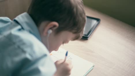 cu boy do school homework writes ballpoint pen in notebook in the ears are inserted headphones