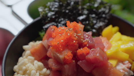 sprinkling sesame seeds on poke bowl with fresh ahi tuna and tobiko