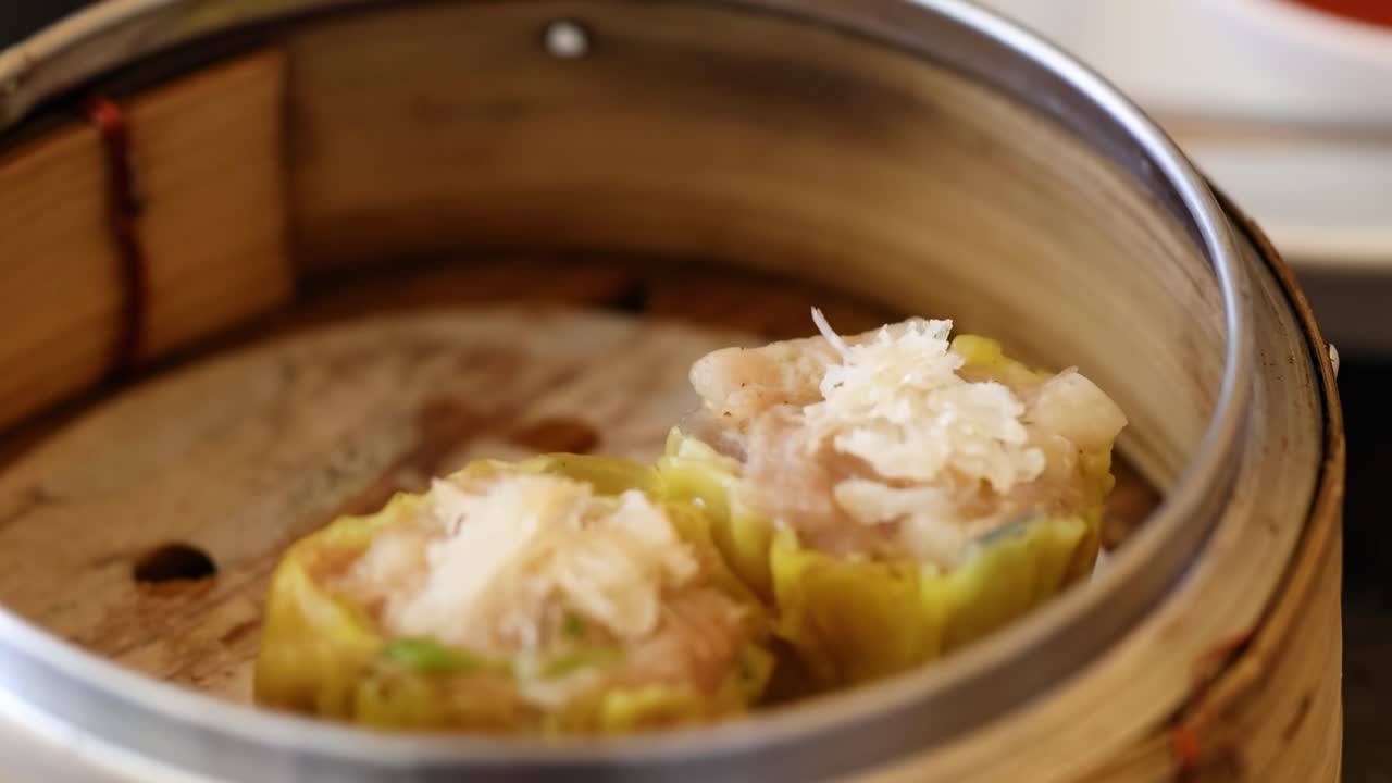 Close-up of chopsticks picking up steamed dumplings from a bamboo steamer, highlighting texture and detail.