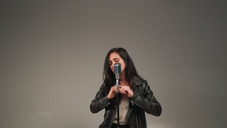 a vocalist in a black leather jacket sings passionately with expressive hands and eyes closed,in front of a vintage microphone.the camera zooms in and out, against a grey background