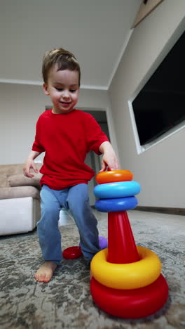 energetic caucasian toddler plays at home. kid jumps up holding a pyramid and watching it fall. low angle view. vertical video.