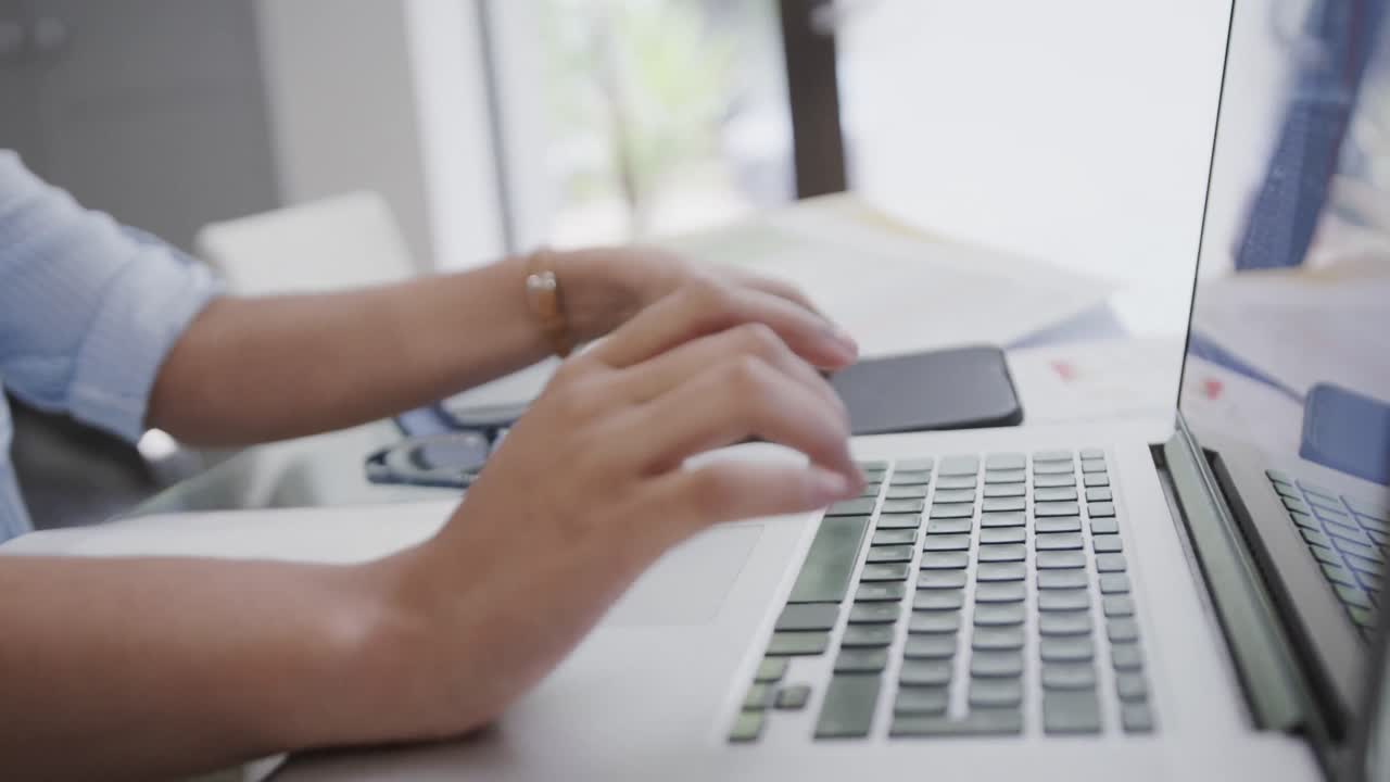 Mezzo busto di donna birazziale indaffarata che usa laptop e smartphone a casa, in slow motion