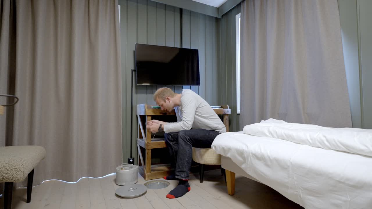 Man lowers fishing gear through hole in hotel floor in Svolvaer, Lofoten, Norway